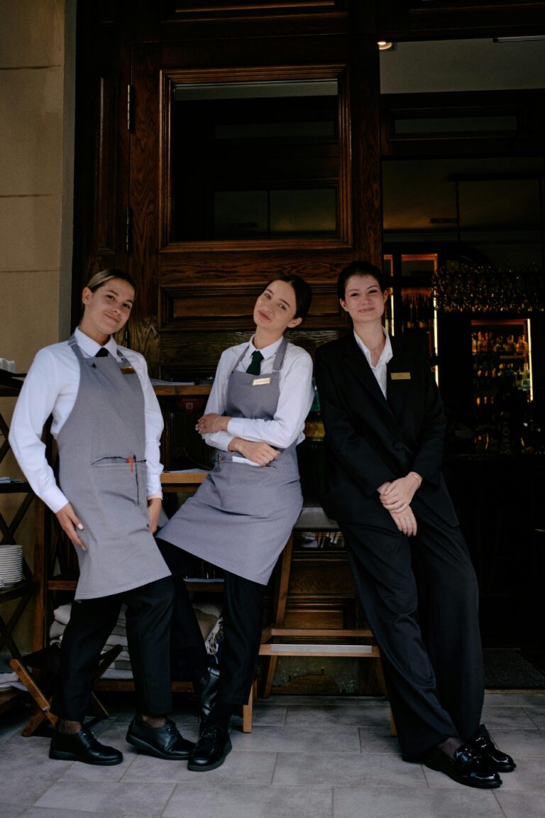 Three restaurant staff members in formal uniforms posing cheerfully in front of a restaurant.